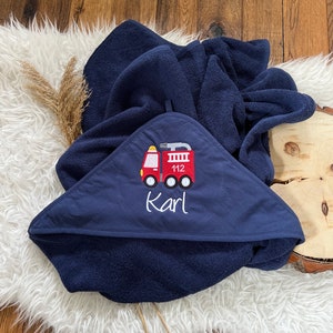 May include: A navy blue hooded towel with a red fire truck embroidered on the front. The fire truck has the number 112 on the side and the name "Karl" is embroidered below it.