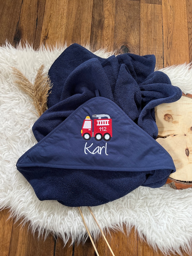 May include: A navy blue hooded towel with a red fire truck embroidered on the front. The fire truck has the number 112 on the side and the name "Karl" is embroidered below it.