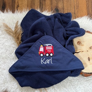 May include: A navy blue hooded towel with a red fire truck embroidered on the front. The fire truck has the number 112 on the side and the name "Karl" embroidered below it.