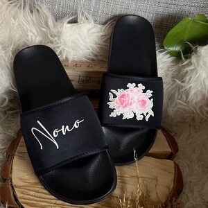 May include: A pair of black slides with a white floral design on one slide and the word "Nono" on the other slide.