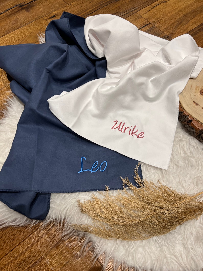 May include: Two personalized fabric squares, one navy blue with the name "Leo" embroidered in blue thread, and one white with the name "Ulrike" embroidered in red thread.