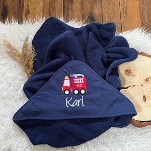 May include: A navy blue hooded towel with a red fire truck embroidered on the front. The fire truck has the number 112 on the side and the name "Karl" is embroidered below it.