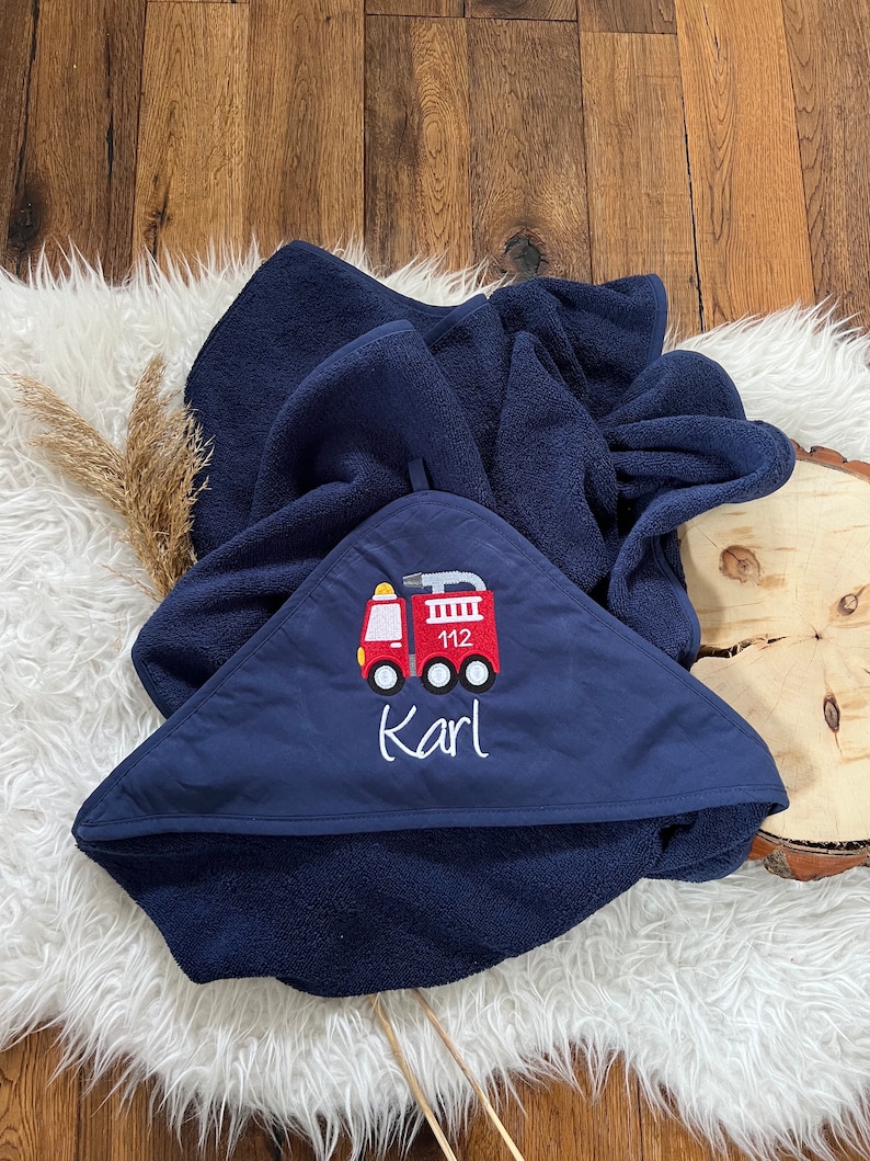 May include: A navy blue hooded towel with a red fire truck embroidered on the front. The fire truck has the number 112 on the side and the name "Karl" is embroidered below it.