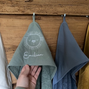 May include: Four hooded towels hanging on hooks. One towel is white, one is green with a lion face and the name "Emilian" embroidered on it, one is blue, and one is yellow.