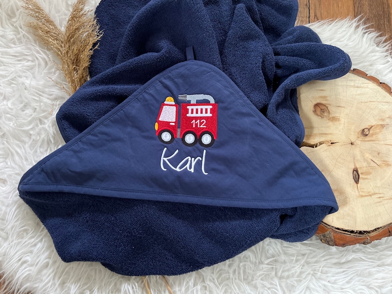 May include: A navy blue hooded towel with a red embroidered fire truck and the name "Karl" on it.