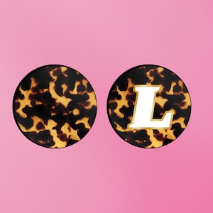 May include: Two round, tortoiseshell patterned hair clips. One clip has a white letter "L" on it.