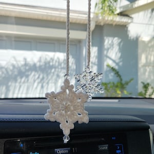 May include: A white crocheted snowflake hanging from the rearview mirror of a car. The car's radio display shows the word "CHILL" on the screen.