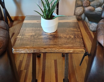 May include: A rustic wooden end table with a live edge top and black metal legs. The table is sitting on a wood floor and has a potted plant on top.