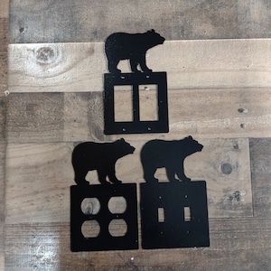 May include: Three black metal light switch covers with bear silhouettes. The top cover has a single bear, the middle cover has two bears, and the bottom cover has a single bear.