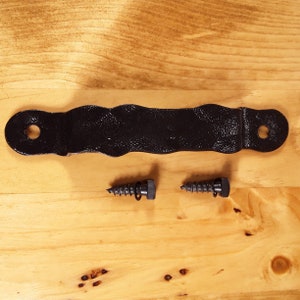 May include: Black metal door handle with a wavy design and two black screws.