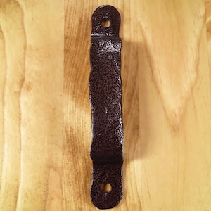 May include: A dark brown metal door handle with a wavy design. The handle has a textured finish and two holes for mounting.