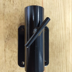 May include: Black metal wall mount with a round pipe and a horizontal bar. The mount is designed to hold a pole or rod.