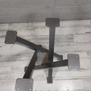 Op de afbeelding: Een metalen tafelonderstel met een stervormig ontwerp. De basis is gemaakt van donkergrijs metaal met vier poten en montageplaten. De poten zijn schuin en in het midden aan elkaar gelast.