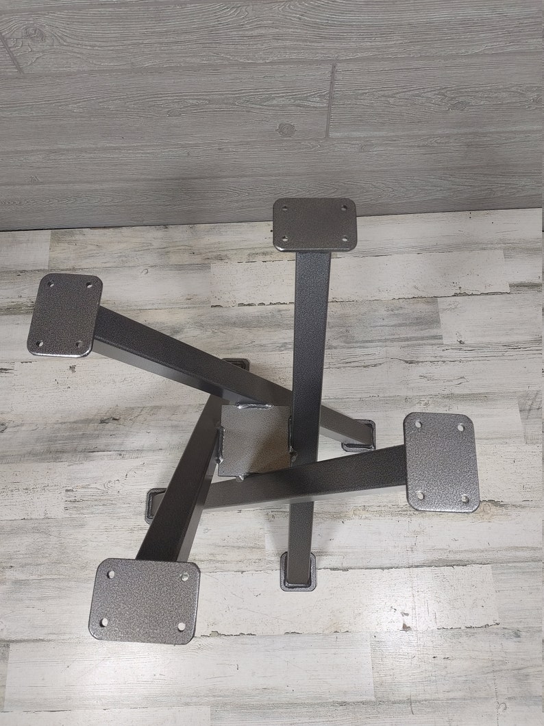 Op de afbeelding: Een metalen tafelonderstel met een stervormig ontwerp. De basis is gemaakt van donkergrijs metaal met vier poten en montageplaten. De poten zijn schuin en in het midden aan elkaar gelast.
