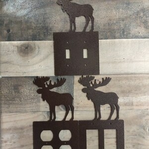 May include: Three metal moose silhouettes in brown with a textured finish. The moose are mounted on top of three different light switch covers. The switch covers are also brown with a textured finish. The top switch cover has two toggle switches, the middle switch cover has four toggle switches, and the bottom switch cover has two toggle switches.