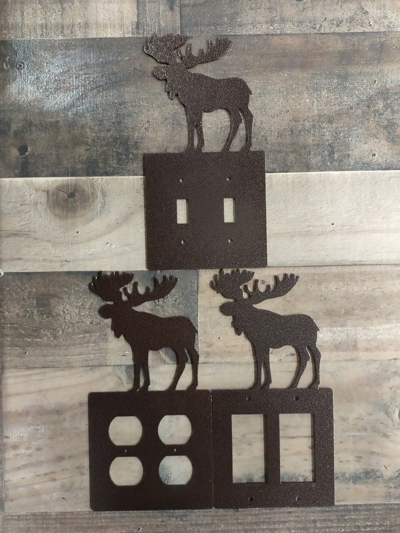 May include: Three metal moose silhouettes in brown with a textured finish. The moose are mounted on top of three different light switch covers. The switch covers are also brown with a textured finish. The top switch cover has two toggle switches, the middle switch cover has four toggle switches, and the bottom switch cover has two toggle switches.