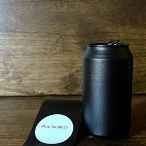 May include: A black, cylindrical can with a pull-tab lid, next to a black, curved metal piece with a white sticker that reads "Black Tex BK-59". The can and metal piece are on a wooden surface.