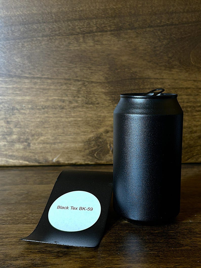 May include: A black, cylindrical can with a pull-tab lid, next to a black, curved metal piece with a white sticker that reads "Black Tex BK-59". The can and metal piece are on a wooden surface.