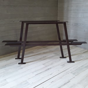 May include: Two black metal table legs with a simple A-frame design. The legs are made of sturdy metal and have a dark brown finish.