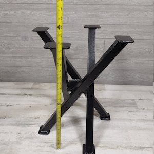 Op de afbeelding: Zwarte metalen tafelpoten met een uniek X-vormig ontwerp. De poten worden gemeten met een gele meetlint, met een hoogte van ongeveer 74 cm. De poten hebben een vierkante basis en bovenste montageplaten.