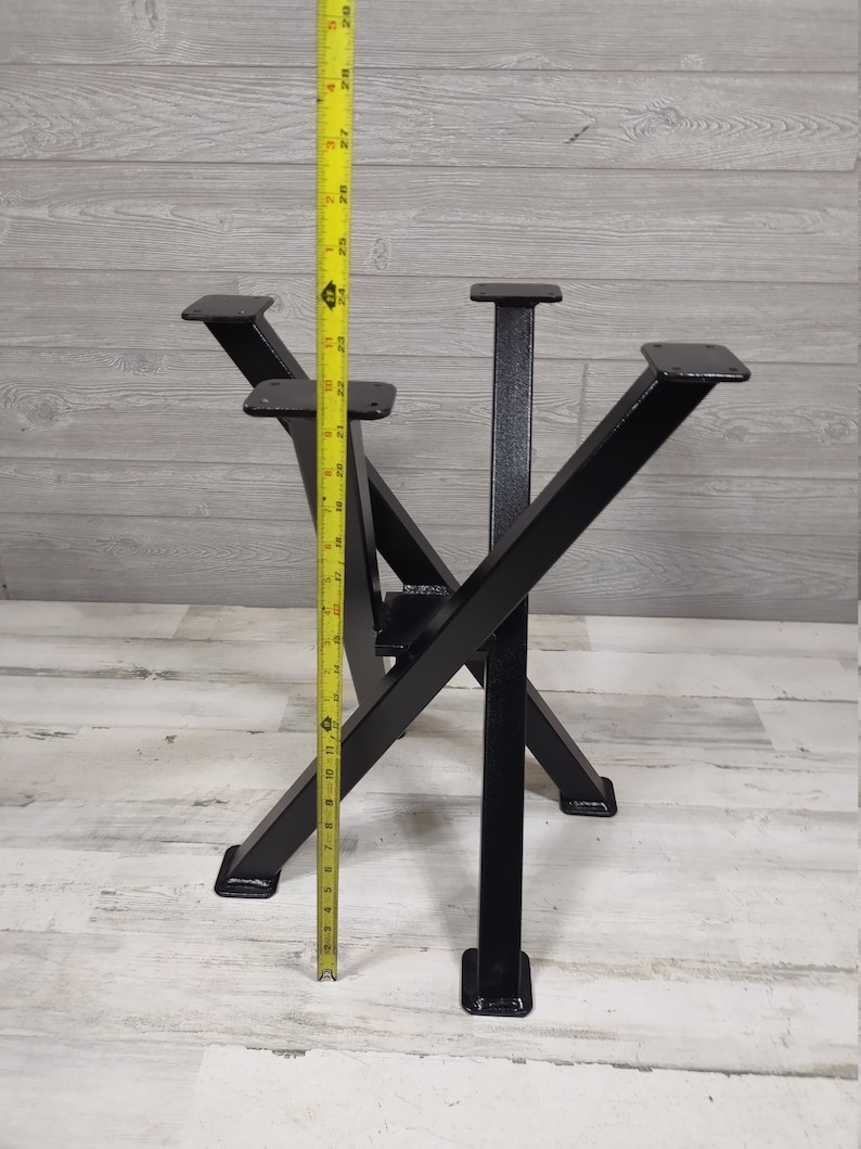 Op de afbeelding: Zwarte metalen tafelpoten met een uniek X-vormig ontwerp. De poten worden gemeten met een gele meetlint, met een hoogte van ongeveer 74 cm. De poten hebben een vierkante basis en bovenste montageplaten.