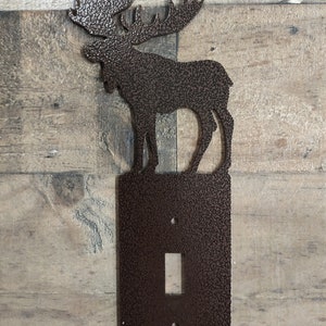 May include: A brown metal light switch cover with a moose silhouette on top. The moose is facing left and has a textured finish.