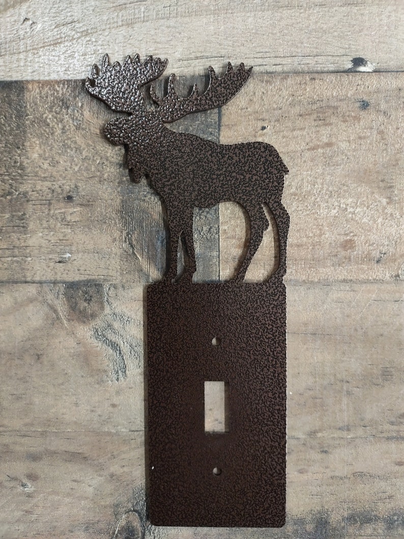 May include: A brown metal light switch cover with a moose silhouette on top. The moose is facing left and has a textured finish.