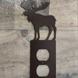 May include: A brown metal moose silhouette wall plate with a double outlet cover. The moose is standing on a textured brown plate with a double outlet cover.