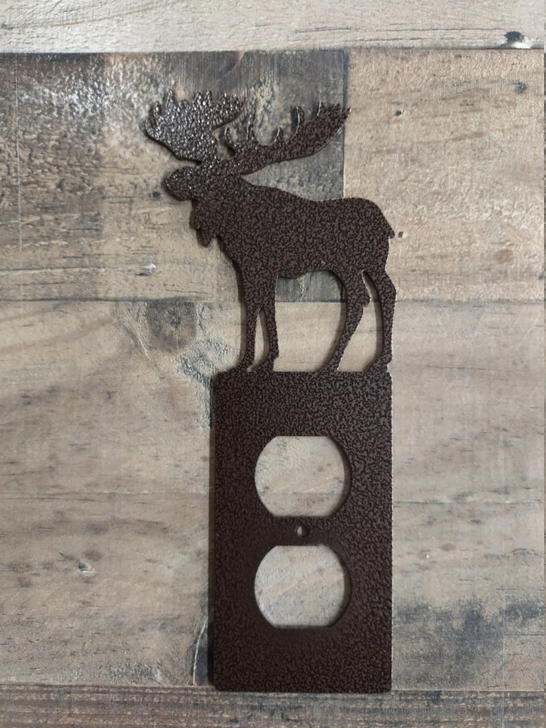 May include: A brown metal moose silhouette wall plate with a double outlet cover. The moose is standing on a textured brown plate with a double outlet cover.