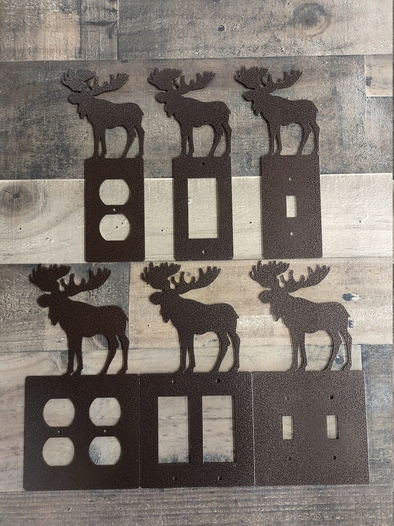 May include: Six metal light switch covers with moose silhouettes. The covers are in a rustic brown color and feature different switch configurations: a double outlet, a single switch, a double switch, a triple switch, and two single switches.