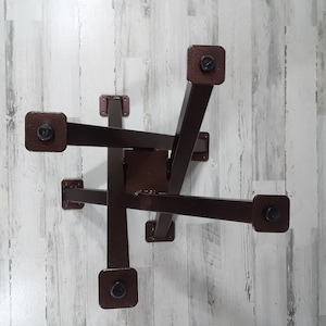 Op de afbeelding: Een bruine metalen tafelvoet met een geometrisch ontwerp. De voet heeft een centrale vierkante steun met zes rechthoekige armen die naar buiten uitsteken, elk eindigend in een vierkante voet. De armen zijn verbonden met bouten.