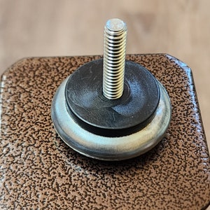 May include: Close-up of a silver metal screw with a black rubber washer and a silver metal base. The screw is threaded and has a rounded head.