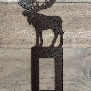 May include: A brown metal moose silhouette wall plate cover for a light switch. The moose is standing on a rectangular plate with a cutout for a light switch.