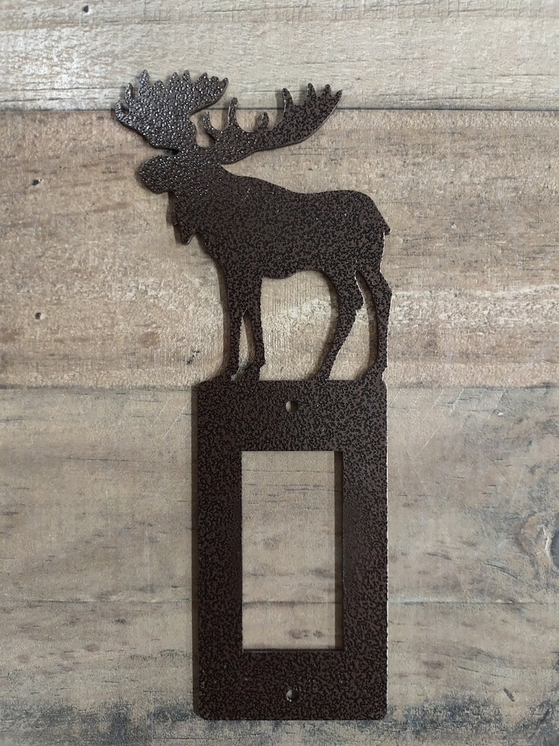 May include: A brown metal moose silhouette wall plate cover for a light switch. The moose is standing on a rectangular plate with a cutout for a light switch.
