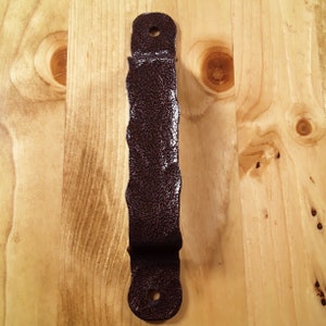 May include: A dark brown metal door handle with a textured finish. The handle has a rounded top and bottom and a slightly curved shape.