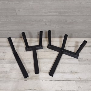 May include: Three black metal stands with a T-shaped base and three vertical supports. The stands are designed to hold items upright.