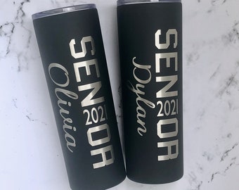 May include: Two black insulated tumblers with silver lettering. One tumbler says "Senior 2021 Olivia" and the other says "Senior 2021 Dylan".