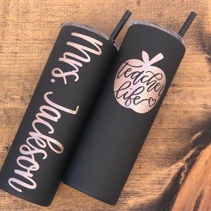 20 oz matte black stainless steel tumbler with custom glitter rose gold decal. Tumbler includes name and apple design on opposite side of tumbler. Tumblers are good for HOT or COLD liquids and can be used with or without straw that is provided.