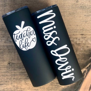 20 oz matte black stainless steel tumbler with custom solid white decal. Tumbler includes name and apple design on opposite side of tumbler. Tumblers are good for HOT or COLD liquids and can be used with or without straw that is provided.