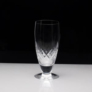 Peut inclure: Un verre en cristal transparent avec un motif de cristal taillé. Le verre a une base large et un corps haut et fin.