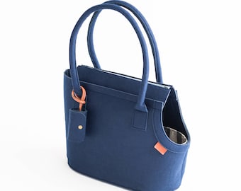 May include: A dark blue felt pet carrier bag with a top handle and a small pocket on the front. The bag has a brown leather trim and a gold metal clasp.
