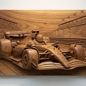 Puede incluir: Tallado en madera detallado de un coche de carreras de Fórmula 1 corriendo por una pista. La obra de arte presenta el logotipo de Petronas y un piloto en la cabina. La escultura en relieve está hecha de madera marrón claro e incluye la pista y la tribuna.