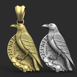 Puede incluir: Se muestran dos colgantes de cuervo, uno dorado y otro plateado. Cada cuervo está posado sobre un emblema circular con símbolos grabados. Los colgantes tienen un diseño detallado en tres dimensiones.