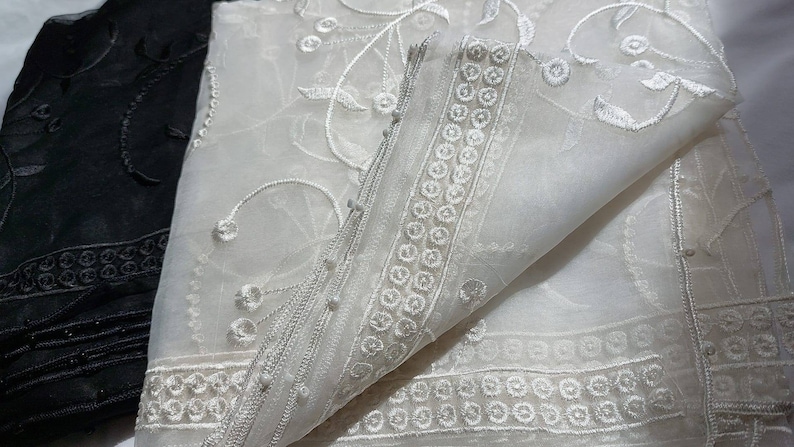 May include: Two sheer fabric scarves, one black and one white, with delicate floral embroidery. The white scarf has a border of small circles.