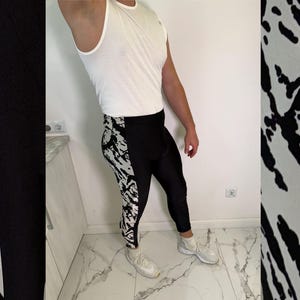 Könnte beinhalten: Ein weißes ärmelloses Tanktop kombiniert mit einer schwarzen Sportleggings, die an den äußeren Seitenteilen ein markantes weiß-schwarzes Marmor- oder Spritzmuster aufweist. Die Leggings ist eng anliegend, reicht bis zu den Knöcheln und wird mit weißen Socken und weißen Sportschuhen getragen.