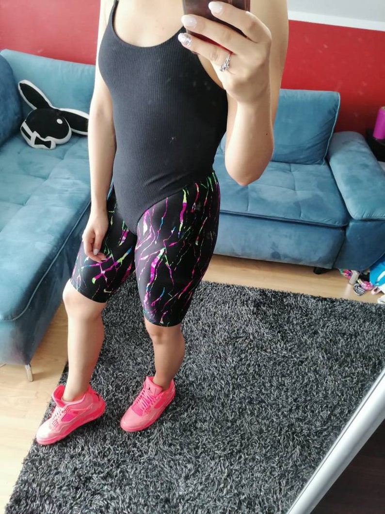 May include: A person wearing a black bodysuit with a colorful abstract print on the shorts. They are wearing pink sneakers.