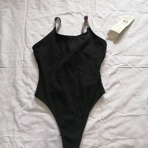 May include: Black bodysuit with thin rainbow straps. The straps are made of a woven fabric.