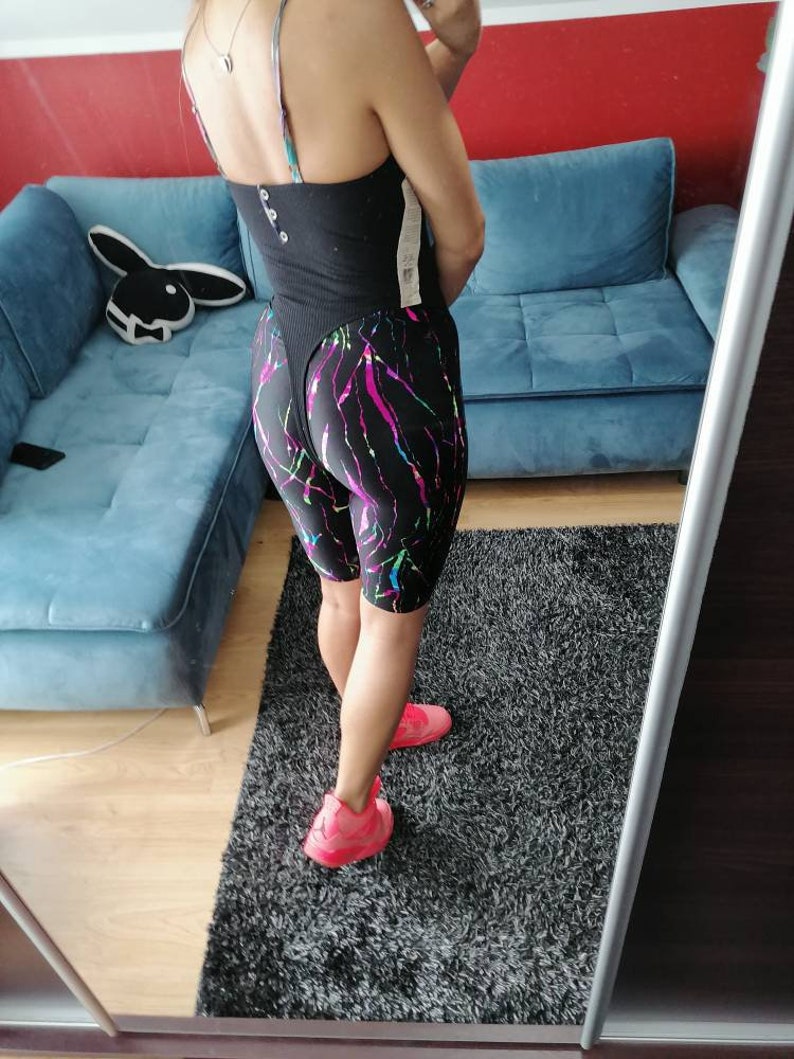 May include: A black bodysuit with a plunging neckline and a colorful abstract print on the shorts. The person is wearing pink sneakers.
