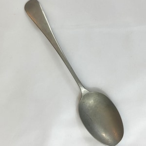 Puede incluir: Una cuchara de plata con un mango largo y delgado y un cuenco ovalado redondeado.