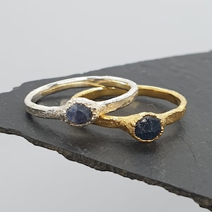 May include: Two rings with a dark blue gemstone set in a textured silver and gold band.